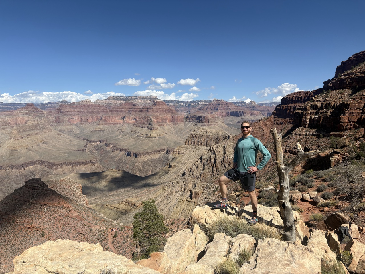 James standing on a rock outcrop below the rim of the Grand Canyon, canyon walls stretching to the horizon
